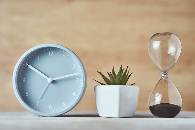 Reloj de arena, reloj despertador y planta en la mesa, cerrar