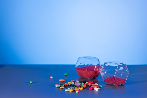 Reloj de arena rojo acostado junto a un puñado de pastillas y pastillas. El concepto de farmacología.