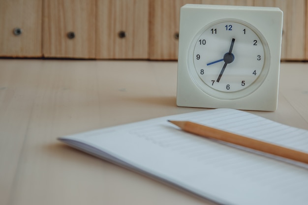 Reloj blanco puesto cerca de cuaderno y lapiz.