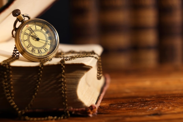 Reloj de bolsillo con cadena y libro en mesa de madera de primer plano Espacio para texto