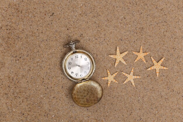 Reloj de bolsillo dorado perdido en la arena con estrella de mar. Vista superior