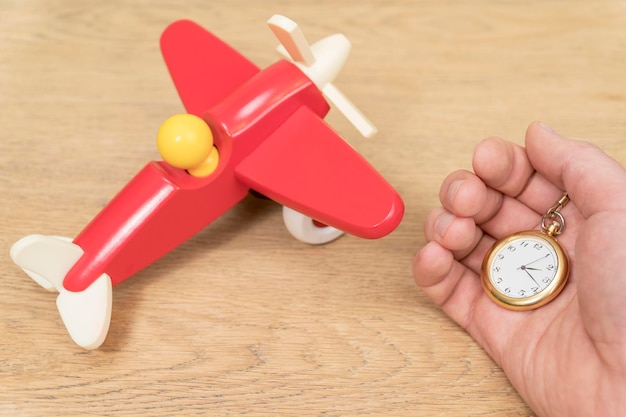 reloj de bolsillo en mano masculina sobre una mesa de madera junto a un avión de juguete