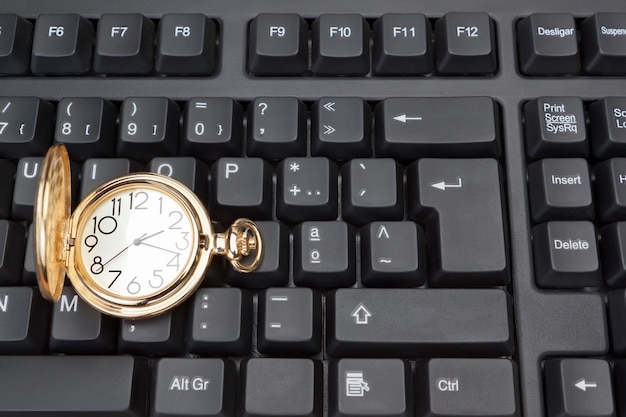 Reloj de bolsillo de oro contra el fondo de un teclado de computadora.