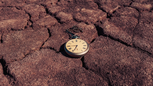 Reloj de bolsillo reloj antiguo vintage retro, mentira sobre un fondo de tierra seca. El concepto de tiempo pasado o futuro.