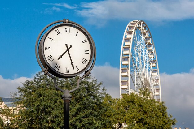 Reloj de la calle y rueda de la fortuna en el parque.