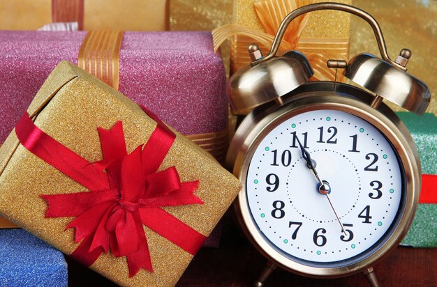 Reloj despertador con árbol de Navidad y regalos en la mesa de madera de cerca