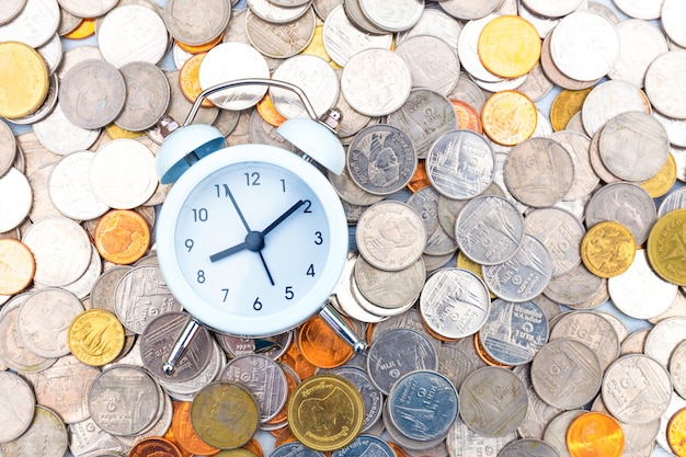 Foto reloj despertador blanco sobre monedas de oro y plata.