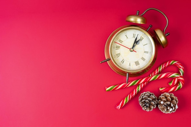 Reloj despertador de bronce bastón de caramelo y conos de abeto sobre fondo rojo Fondo de Navidad y Año Nuevo