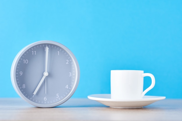 Reloj despertador gris clásico y taza de café con leche en azul