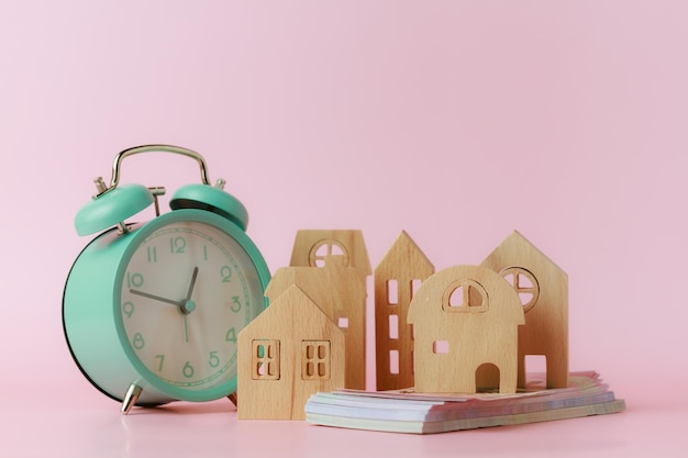 Foto un reloj despertador con modelo de casa de madera y billetes de banco en fondo rosa