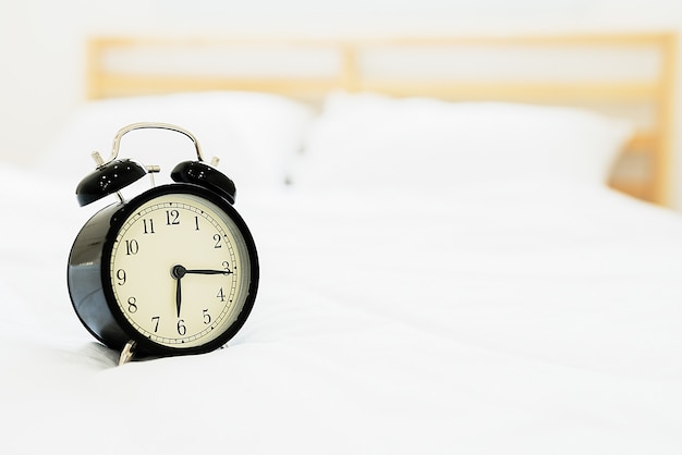 Foto reloj despertador negro en la cama.