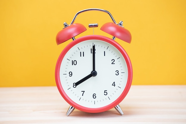 Reloj despertador retro vintage de ocho minutos a las doce en punto en la mesa de madera con pared amarilla.