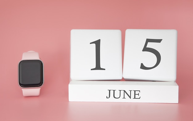 Reloj inteligente con calendario de cubo y fecha 15 de junio en mesa rosa.