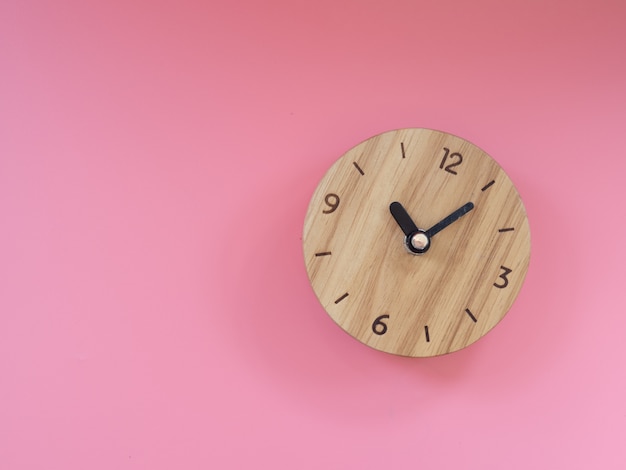 Reloj de madera sobre fondo rosa