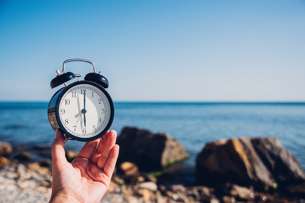 Reloj de mano en el fondo de la playa. Reloj de alarma en el mar y la arena de fondo diferente tiempo con las vacaciones de verano. Concepto de tiempo de vacaciones.