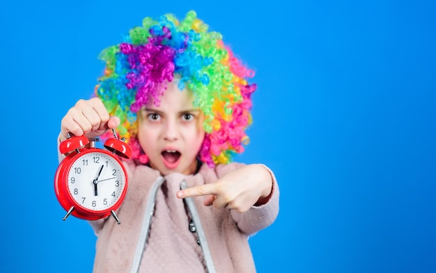 Foto el reloj marca el tiempo adorable niño pequeño con peluca de pelo de colores apuntando al reloj de alarma para la hora exacta concepto de tiempo mide el tiempo de tu reloj con el espacio de mi copia