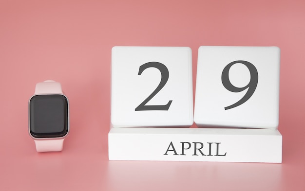 Reloj moderno con calendario cubo y fecha 29 de abril sobre fondo rosa. Concepto vacaciones de primavera.