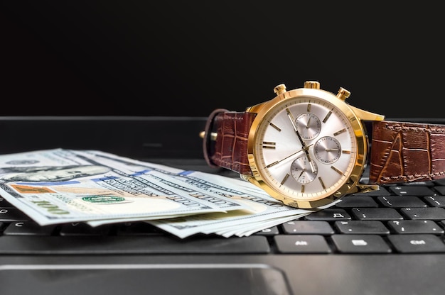 Reloj de pulsera con dinero en el teclado del portátil.