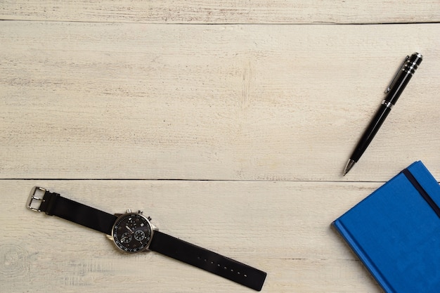 Reloj de pulsera mecánico, diario y bolígrafo se encuentran en una mesa de luz de madera