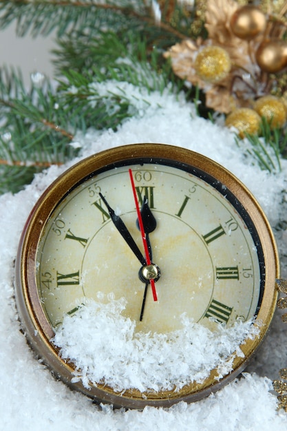 Reloj con ramas de abeto y adornos navideños bajo la nieve de cerca