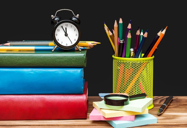 Foto reloj con suministros para alumnos en la mesa de madera sobre fondo de pizarra hora de ir a la escuela