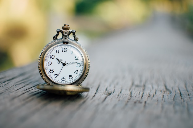 Reloj de la vendimia en la mesa de madera con fondo de naturaleza.