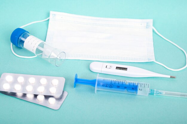 Remédios para resfriado. tubo de ensaio, seringa, pílulas e respirador máscara médica, termômetro sobre fundo azul.