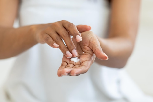 Remedios para la piel seca Mujer afroamericana irreconocible aplicando crema hidratante en las manos