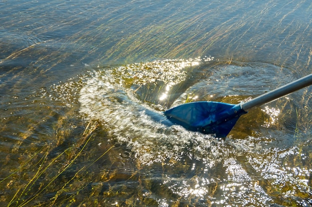 Foto el remo de la embarcación toca el agua y provoca salpicaduras y ondulaciones en el agua. paleta azul y su reflejo en el río mientras navega en un barco, catamarán