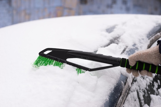 Remoción de nieve, coche en nieve. La mujer limpia el coche de la nieve.