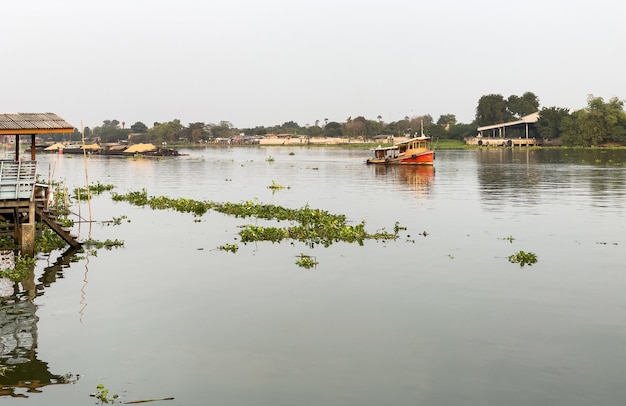 Un remolcador está remolcando el gran bote de carga lleno de arena en el gran río hasta el sitio de construcción cerca del río, vista frontal con el espacio de la copia.