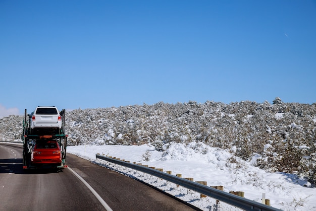 El remolque transporta automóviles en la autopista en invierno con paisaje nevado