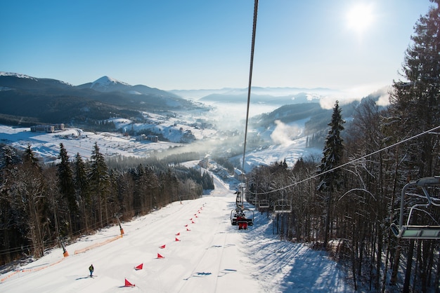 Remonte con esquiadores, pendiente nevada, montañas con un paisaje ideal de terreno cubierto de nieve y neblina sobre él en un día soleado en el resort. Temporada de esquí y concepto de deportes de invierno.