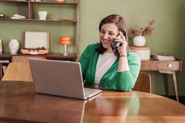 remotamente una mujer trabaja en casa en línea responde una llamada telefónica a un cliente Usa una computadora portátil