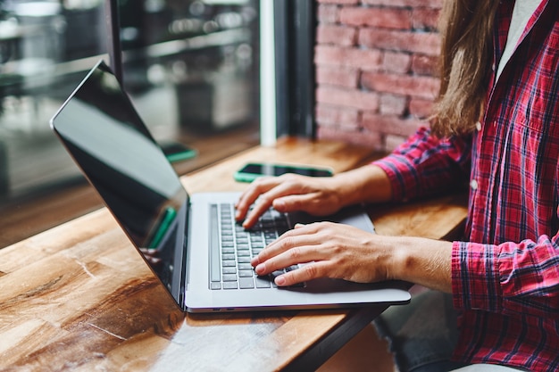 Foto remotamente online inteligente trabalhando em um laptop perto da janela de um café. local de trabalho aconchegante