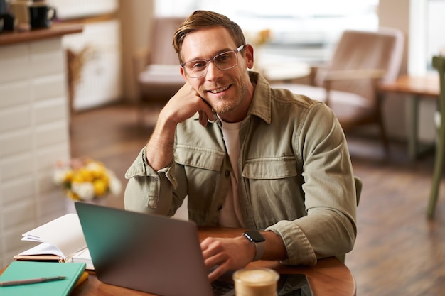 Foto remote-arbeit und freelance-konzept gutaussehender mann in brille sitzt mit notebook und laptop und studiert