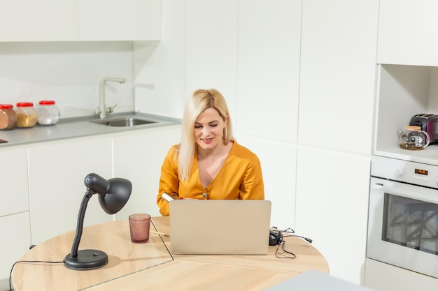 Remote-Arbeiten von zu Hause aus. Junge Frau, die Laptop verwendet. Freiberuflicher Arbeitsplatz im Küchenbüro. Telearbeit in Isolation, weibliches Geschäft, Online-Shopping. Student im Fernstudium. Lifestyle-Moment.