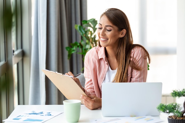 Remote-Job-Technologie und People-Konzept Glücklich lächelnde junge Geschäftsfrau mit Laptop-Computer und Papieren, die im Home Office arbeiten