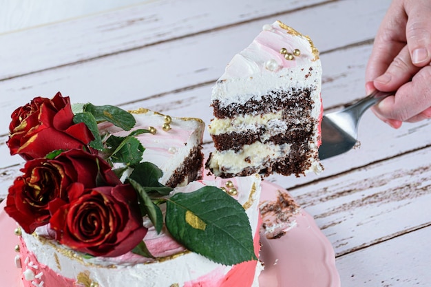 Removendo uma fatia de bolo de chocolate coberto com creme de manteiga de merengue suíço. Três flores vermelhas no topo.