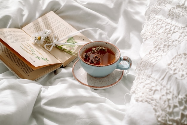 Renda perfurada, manta de algodão branco. livro botânica, caneca com chá de ervas naturais feito de hortelã, flores de margarida de verão. Café da manhã na cama. Provença e estilo retro. Limpe o conforto e o frescor.