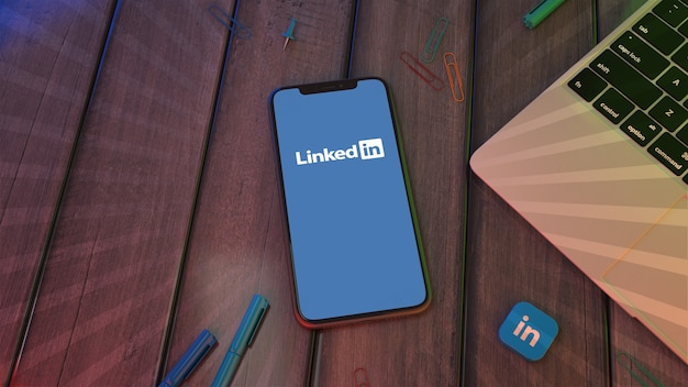 Renderização 3D de um smartphone exibindo o logotipo do aplicativo Linkedin em uma área de trabalho de madeira