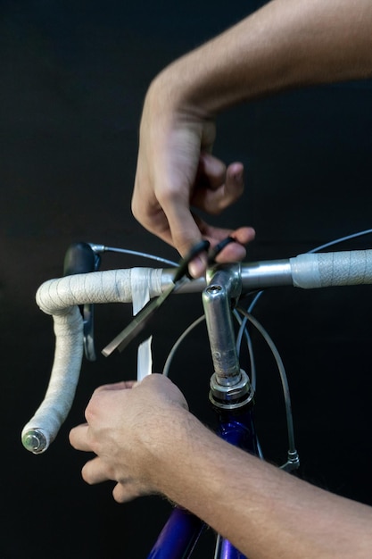 Rennrad-Lenker auf schwarzem Hintergrund Installieren Sie Lenkerband weiß Fahrradreparatur in einer modernen Werkstatt Mechaniker in der Werkstatt Hände und weißes Isolierband Nahaufnahme