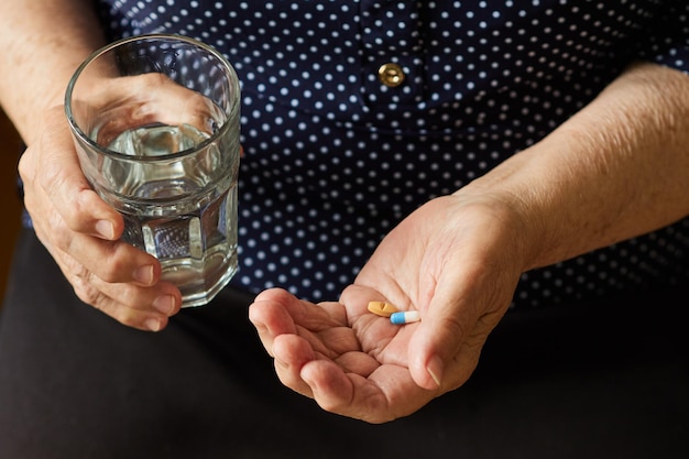 Rentnerin mit einem Glas Wasser wird Pillen einnehmen