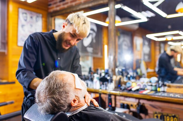 Foto rentnermann mit grauem bart mit friseur im trendigen spa-männerpflegesalon