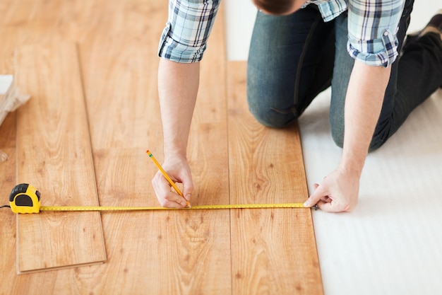 reparação, construção e conceito de casa - close-up de mãos masculinas medindo piso de madeira