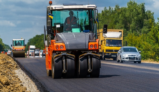 Reparação de estradas, compactador coloca asfalto. Máquinas especiais pesadas. Pavimentadora de asfalto em operação. Vista lateral. Fechar-se.