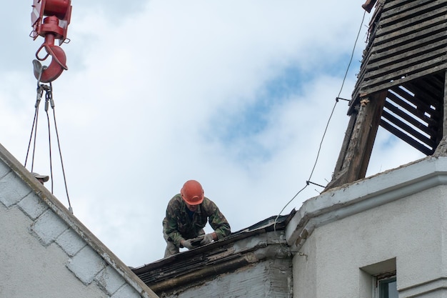 Reparação do telhado de um belo edifício antigo no centro da cidade Trabalho em altura Trabalhadores reparam o telhado substituem as telhas O gancho do guindaste de torre paira sobre as cabeças dos trabalhadores