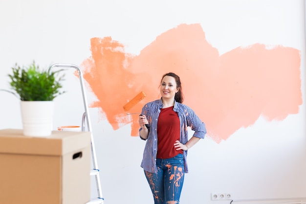 Reparação no apartamento. Mulher feliz pinta a parede com tinta.