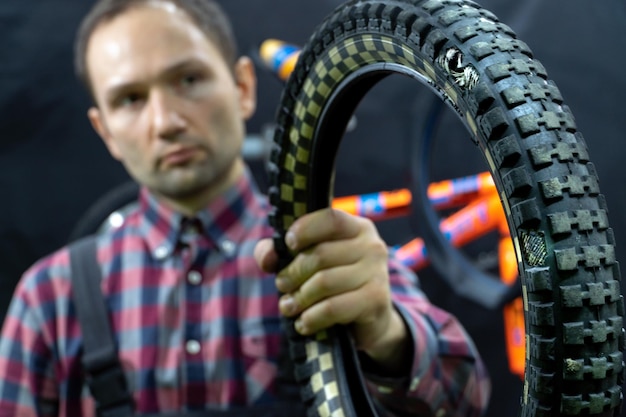 Reparación de una bicicleta para niños en el taller El mecánico sostiene un viejo neumático pinchado con un agujero en la mano Reemplazo de un neumático en una bicicleta Un amable mecánico en el taller