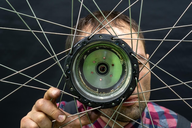 Reparación de bicicletas eléctricas Un mecánico de bicicletas sostiene una rueda con un motor eléctrico y una llave en sus manos Primer plano de rueda de bicicleta sobre un fondo negro